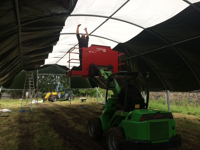 Person using an avant loader to support the roof of a new polytunnel being built.