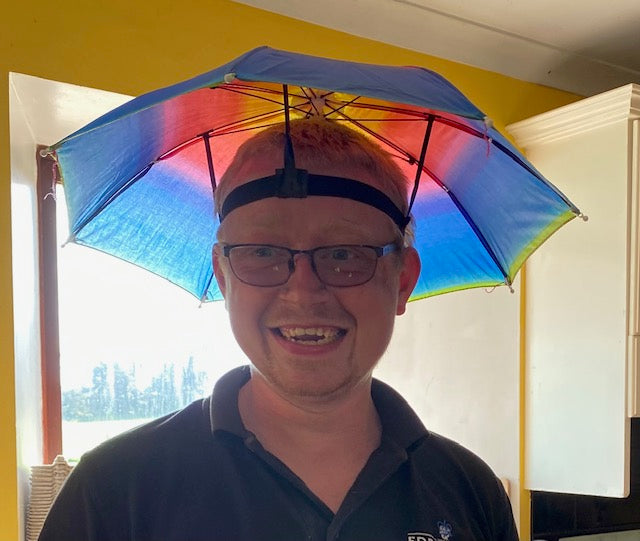 Scott wearing a colorful umbrella on their head indoors.