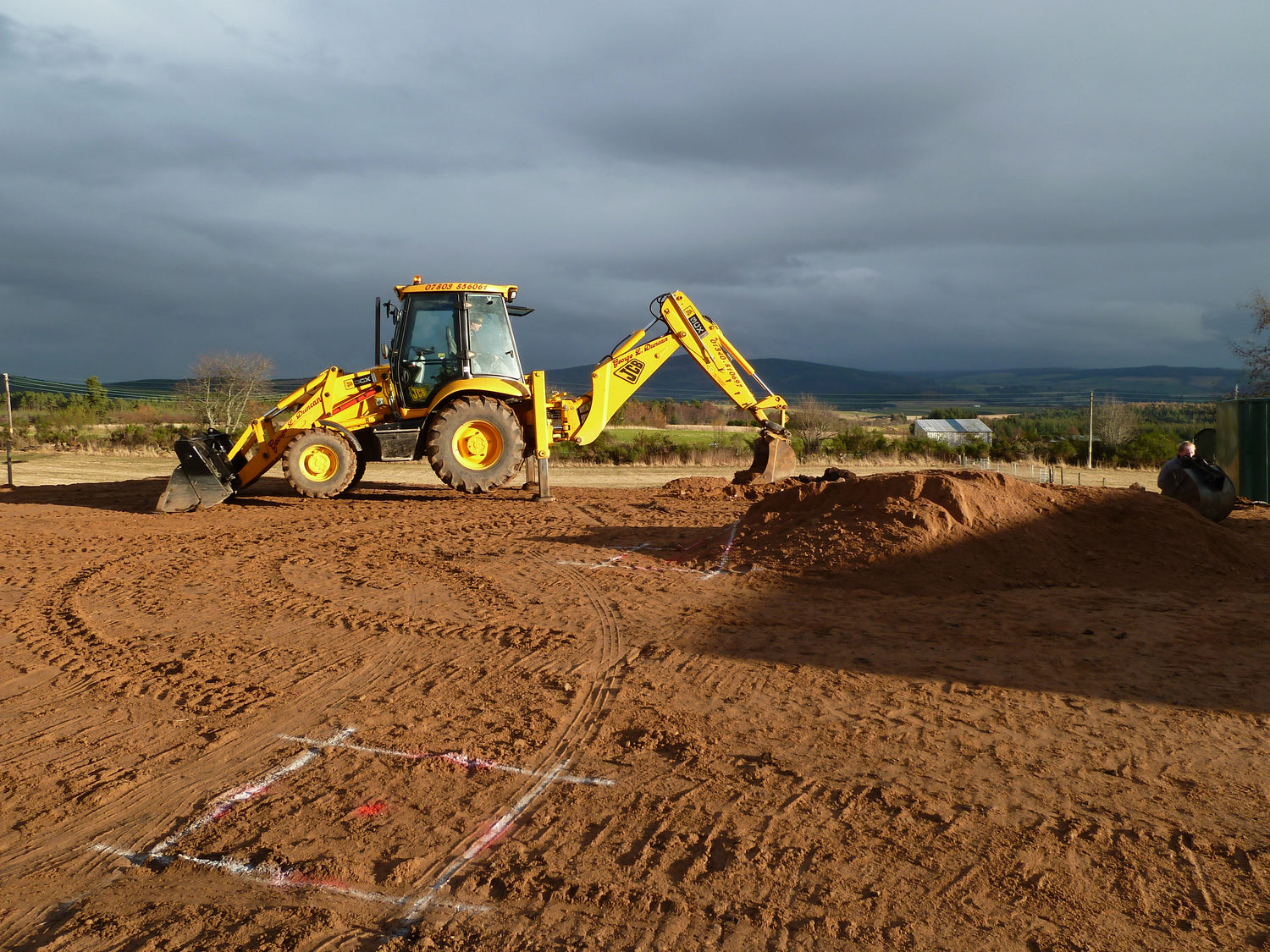 Yellow backhoe loader on a dirt field with a cloudy sky.