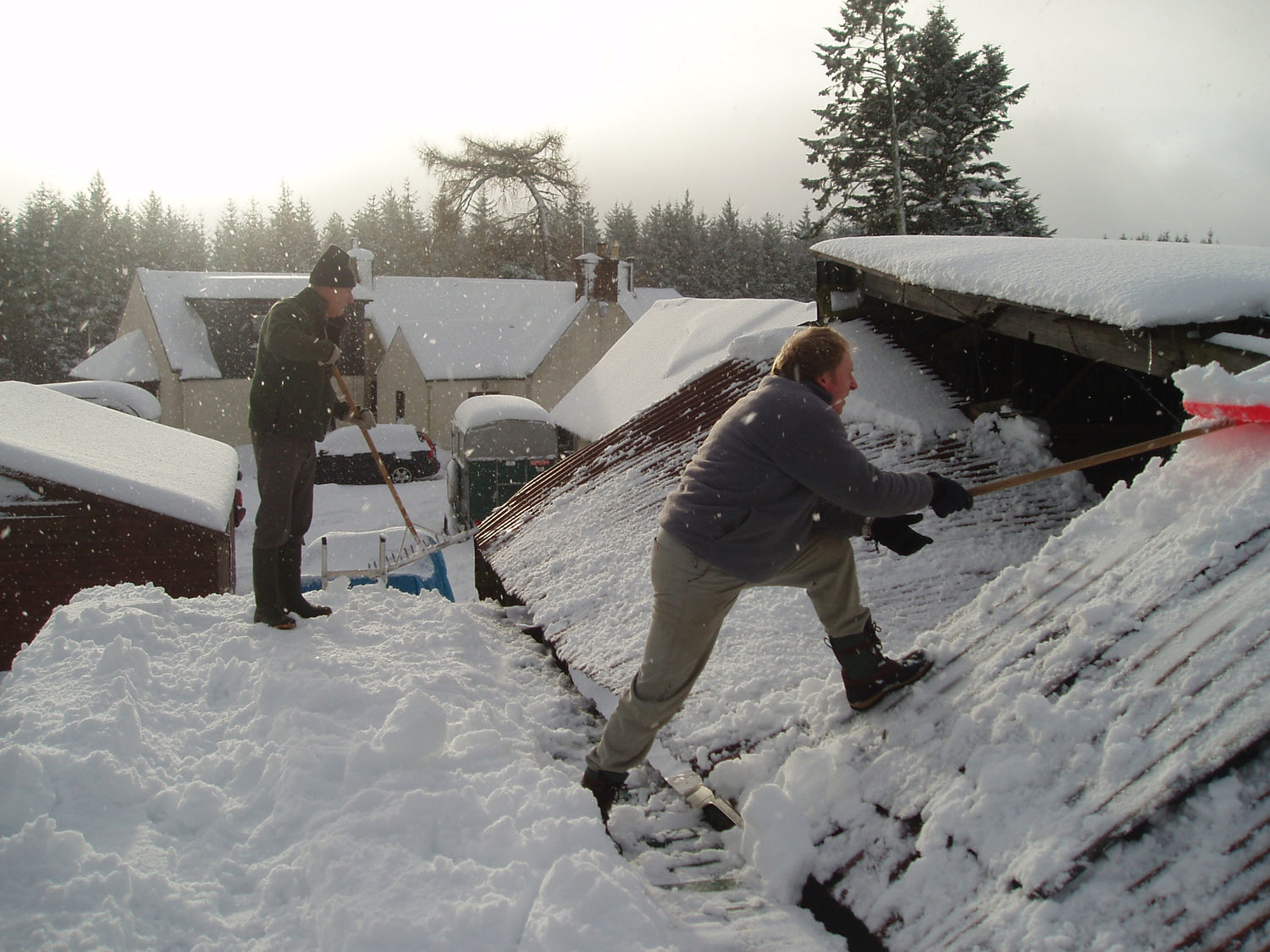 Two people shovelling snow off a collapsing barn roof.